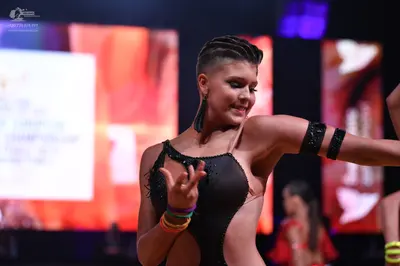 Dancesport competitor: Female dancer in foreground: black latin dance bodysuit with rhinestones and bla