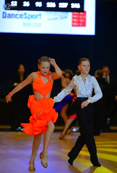 Dancesport competitor: Female dancer: bright orange Latin dance dress with a cutout design and ruffled 