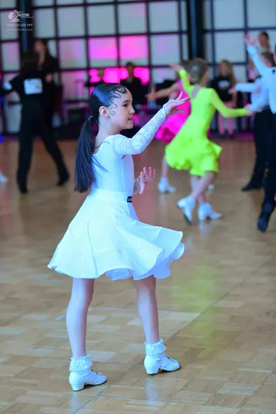 Dancesport competitor: Female dancer in foreground: white long-sleeved dress with lace sleeves and a fl