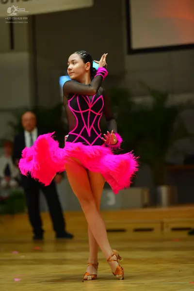 Dancesport competitor: Female dancer: black and bright pink latin dress with long sheer sleeves and pin