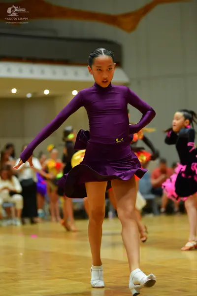 Dancesport competitor: Female dancer in foreground: purple long-sleeved latin dress
