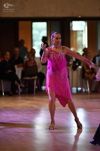 Dancesport competitor: Female dancer: bright pink, one-shoulder Latin dress with rhinestone embellishme