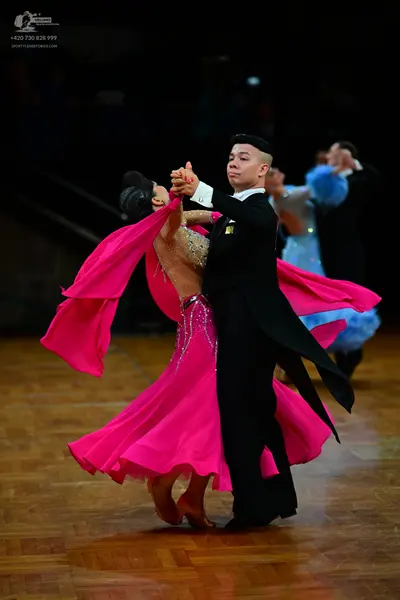 Dancesport competitor: Foreground female dancer: bright pink ballgown with a sequin-embellished bodice 