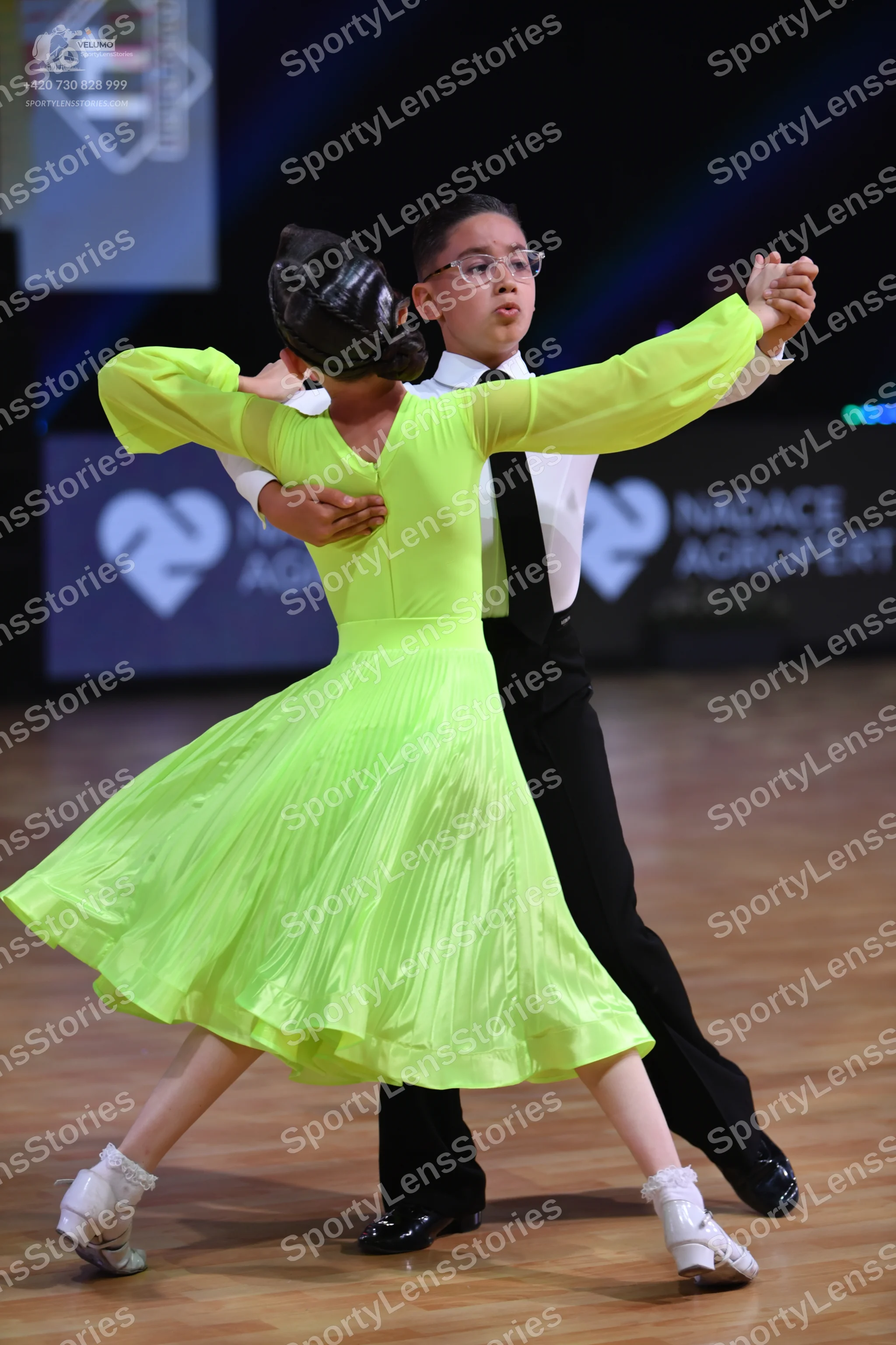Dancesport competitor: Female dancer: lime green long-sleeved dress with a flowing, pleated skirt and w