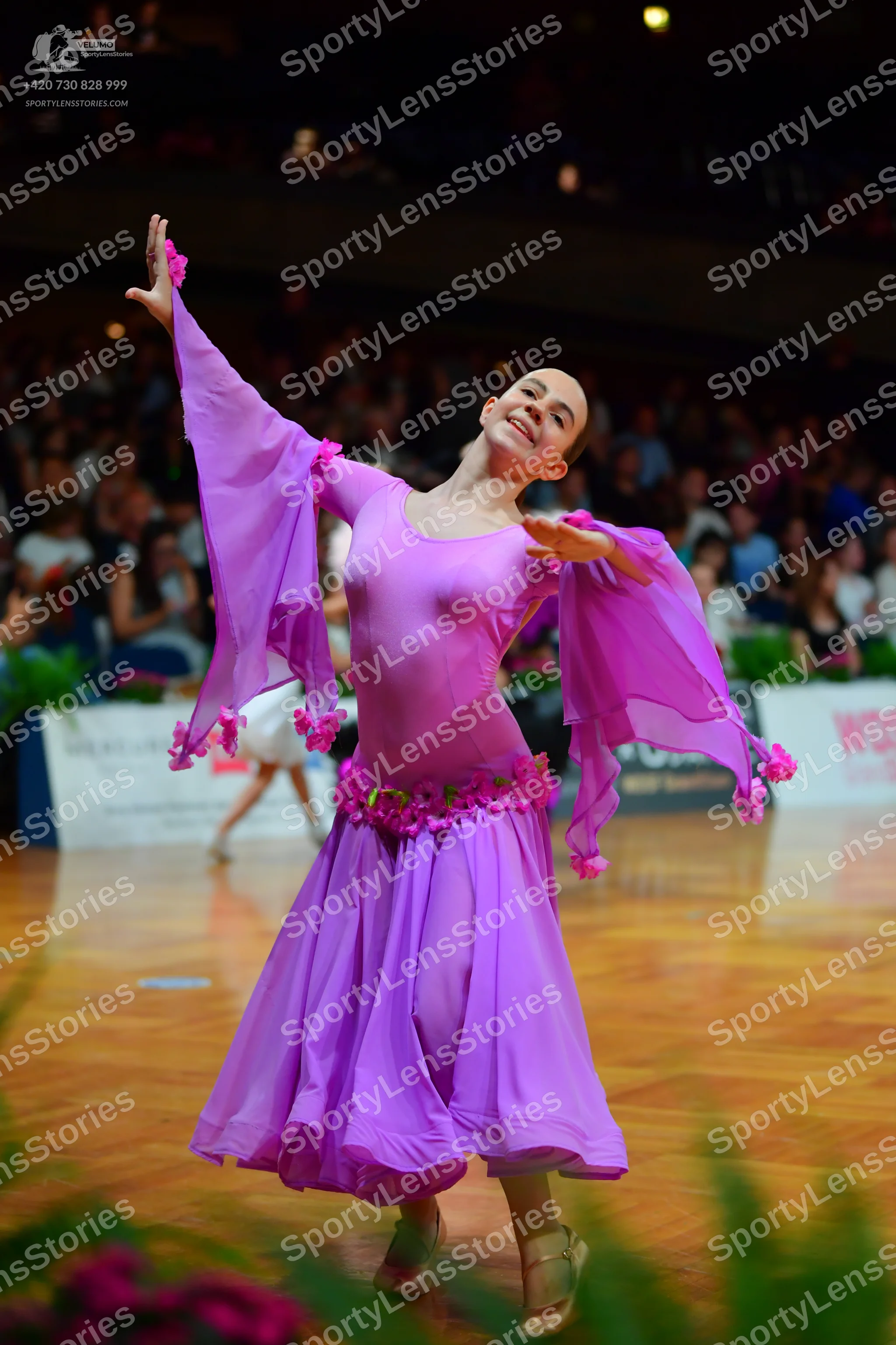 Dancesport competitor: Female dancer in foreground: light purple latin dance dress with long flowing sl