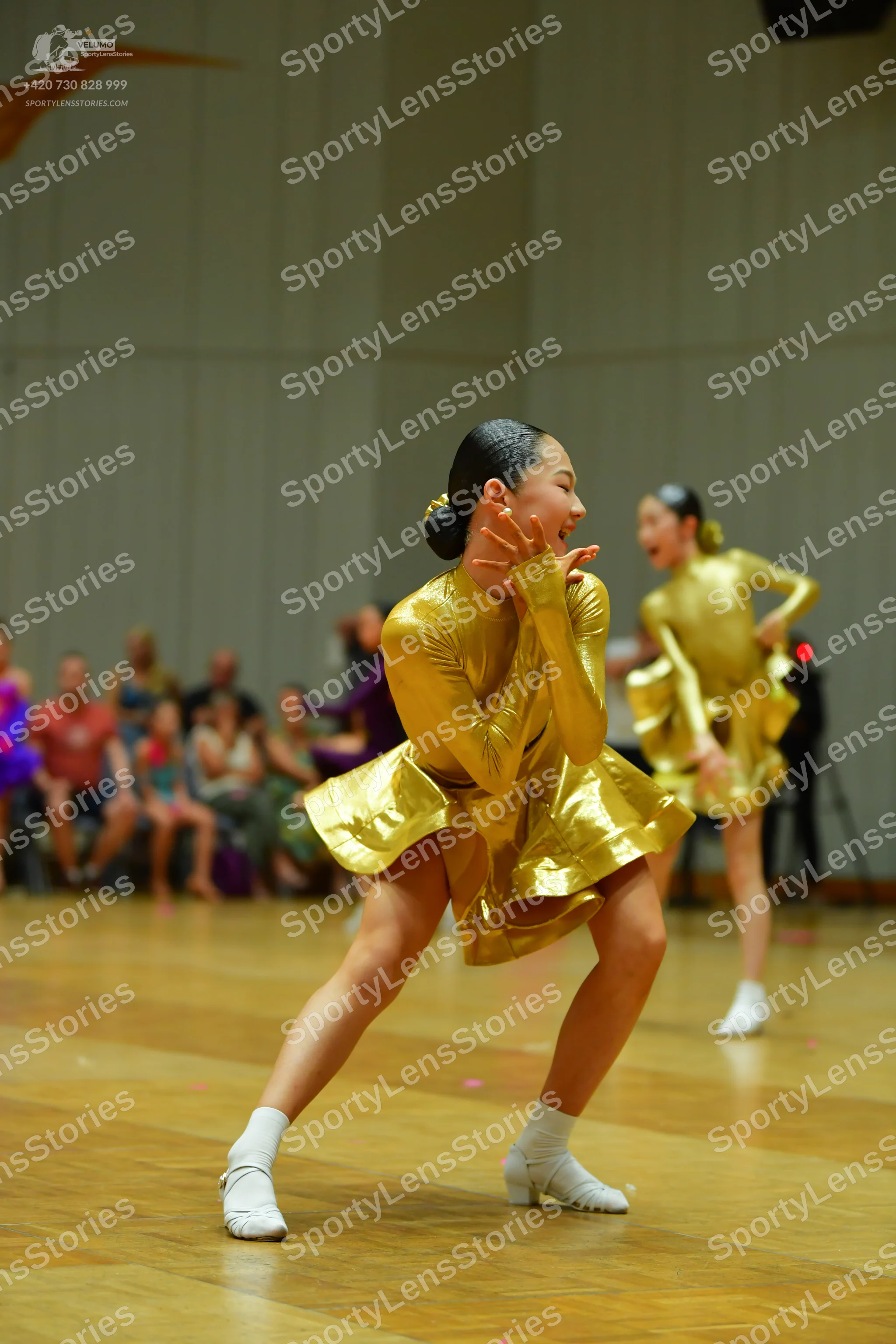 Dancesport competitor: Female dancer in foreground: gold metallic long-sleeved latin dress with a flare