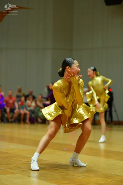 Dancesport competitor: Female dancer in foreground: gold metallic long-sleeved latin dress with a flare