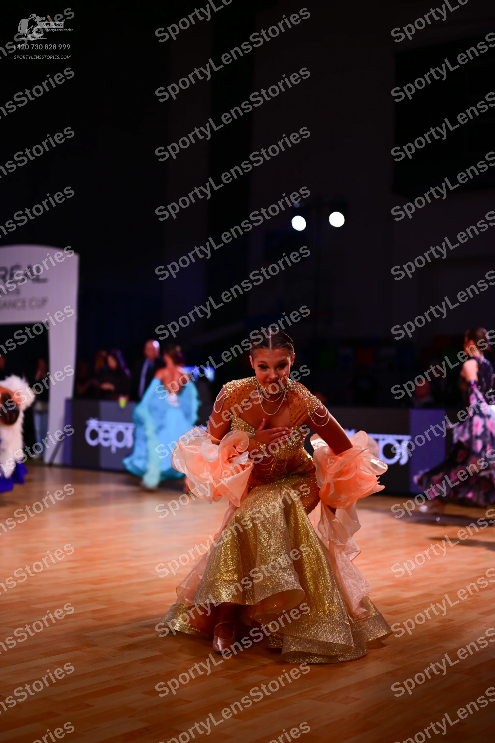 Dancesport competitor: Foreground female dancer: gold/bronze sequined ballgown with large, peach-colore