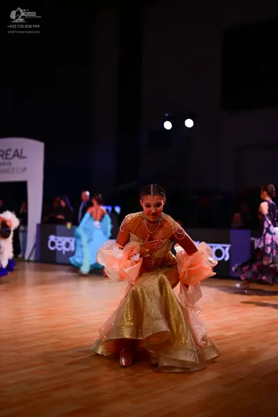 Dancesport competitor: Foreground female dancer: gold/bronze sequined ballgown with large, peach-colore