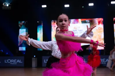 Dancesport competitor: Female dancer in foreground: bright pink Latin dress with extensive fringe or fe