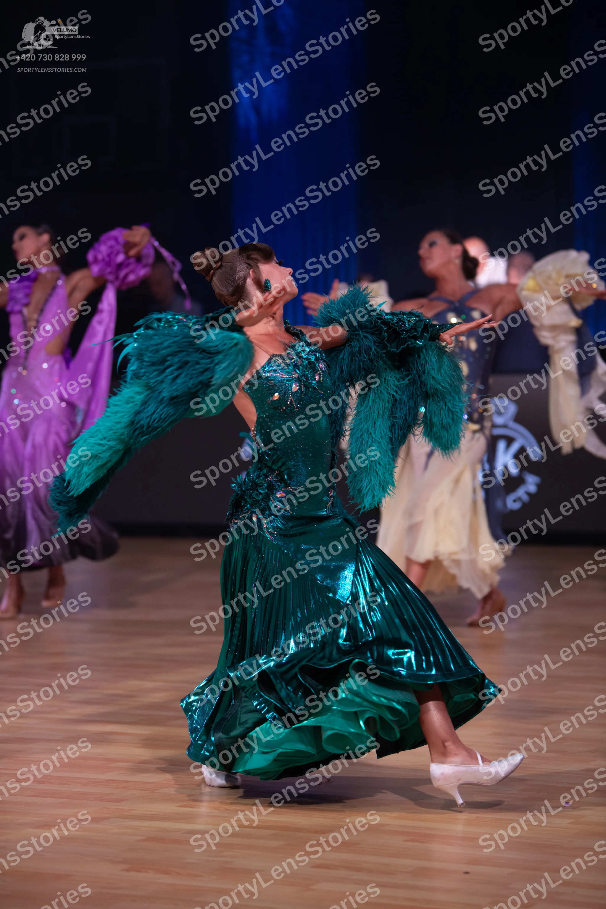 Dancesport competitor: Female dancer in foreground: teal satin dress with a voluminous ruffled skirt an