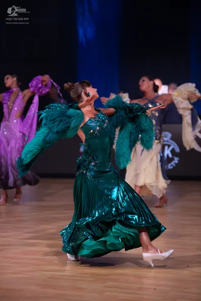 Dancesport competitor: Female dancer in foreground: teal satin dress with a voluminous ruffled skirt an