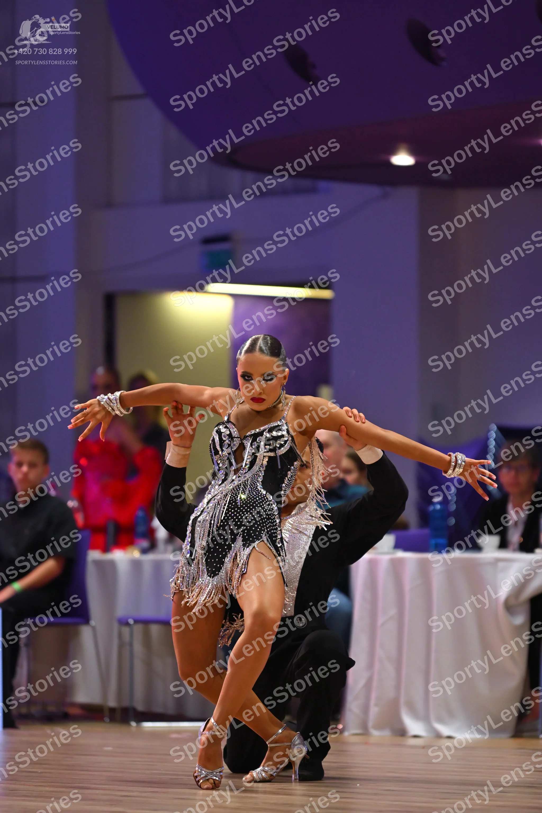 Dancesport competitor: Female dancer: black Latin dress with silver sequins and silver fringe, and larg