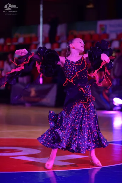 Dancesport competitor: Female dancer: dark navy or black Latin dress with large bright pink polka dots,