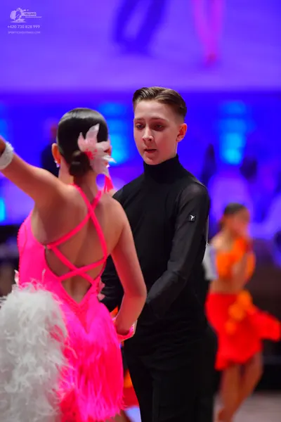 Dancesport competitor: Female dancer in foreground: bright pink latin dress with criss-cross back strap