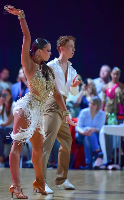 Dancesport competitor: Female dancer: gold sequined Latin dress with long white fringe, gold hoop earri