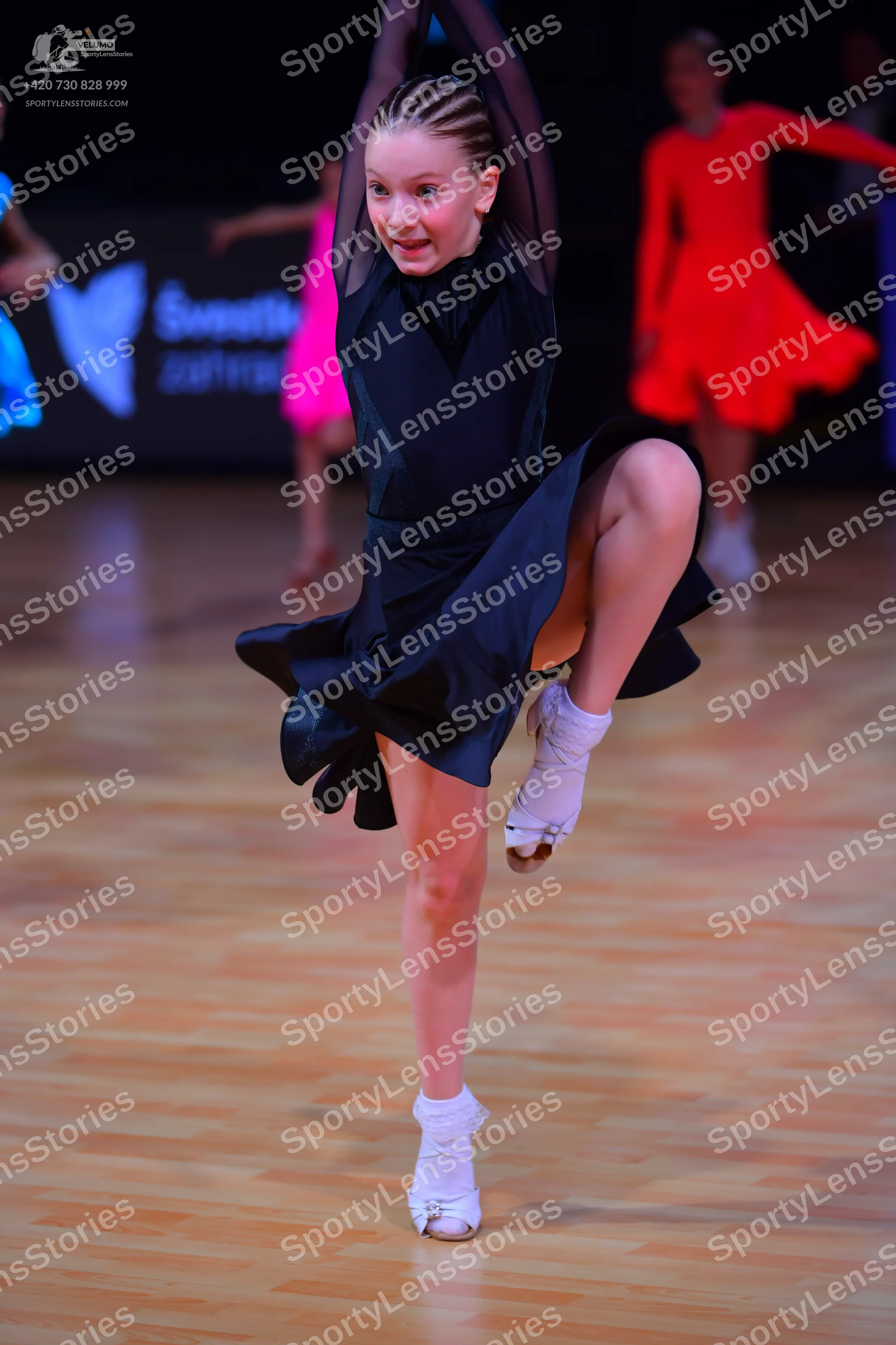 Dancesport competitor: Female dancer in foreground: black latin dress with long sleeves and satin-like
