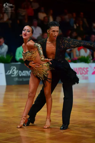 Dancesport competitor: Female dancer: gold latin dress with heavy sequins and fringe, large earrings, a