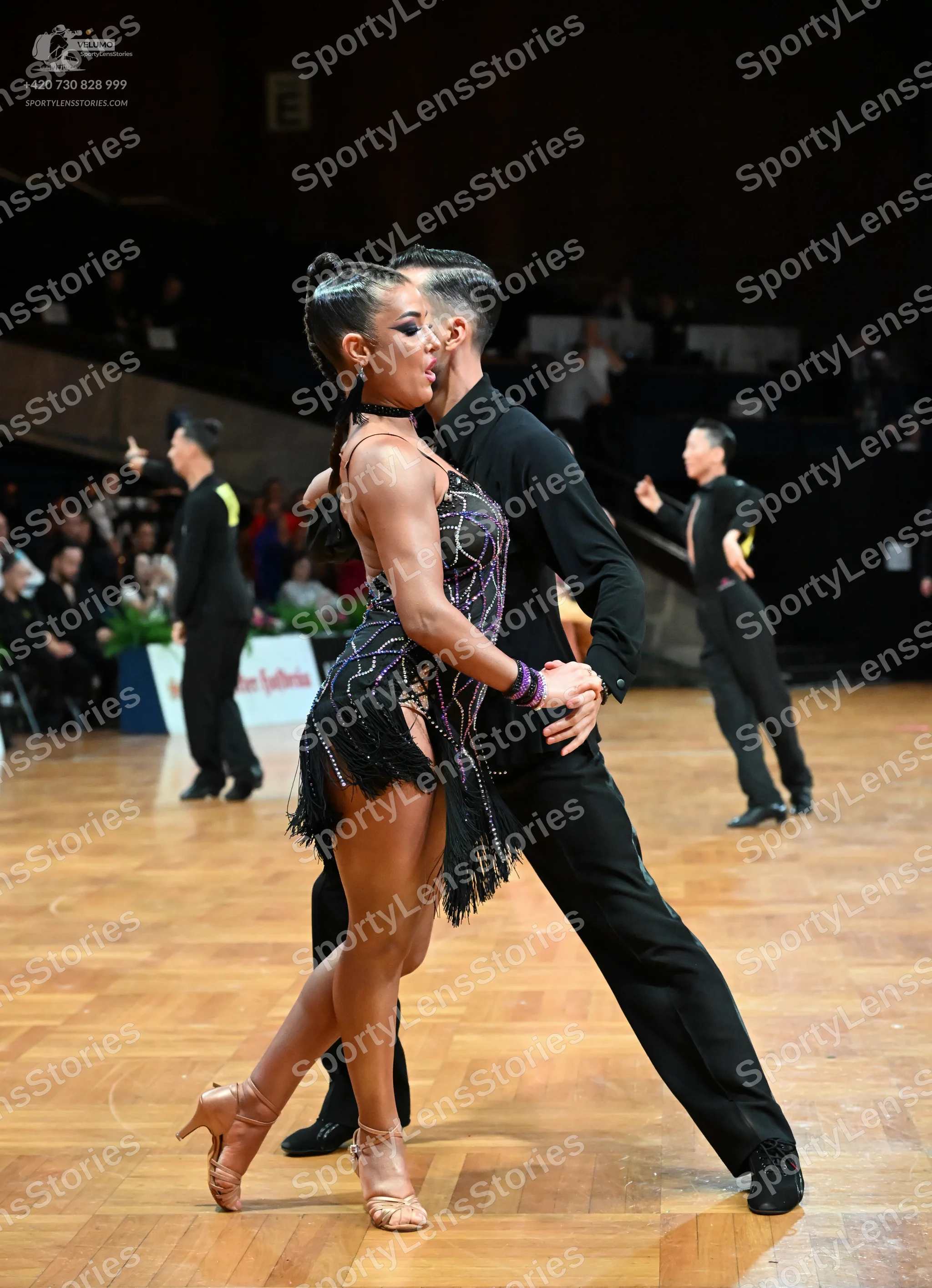 Dancesport competitor: Central female dancer: black sequin Latin dress with black fringe, black choker,
