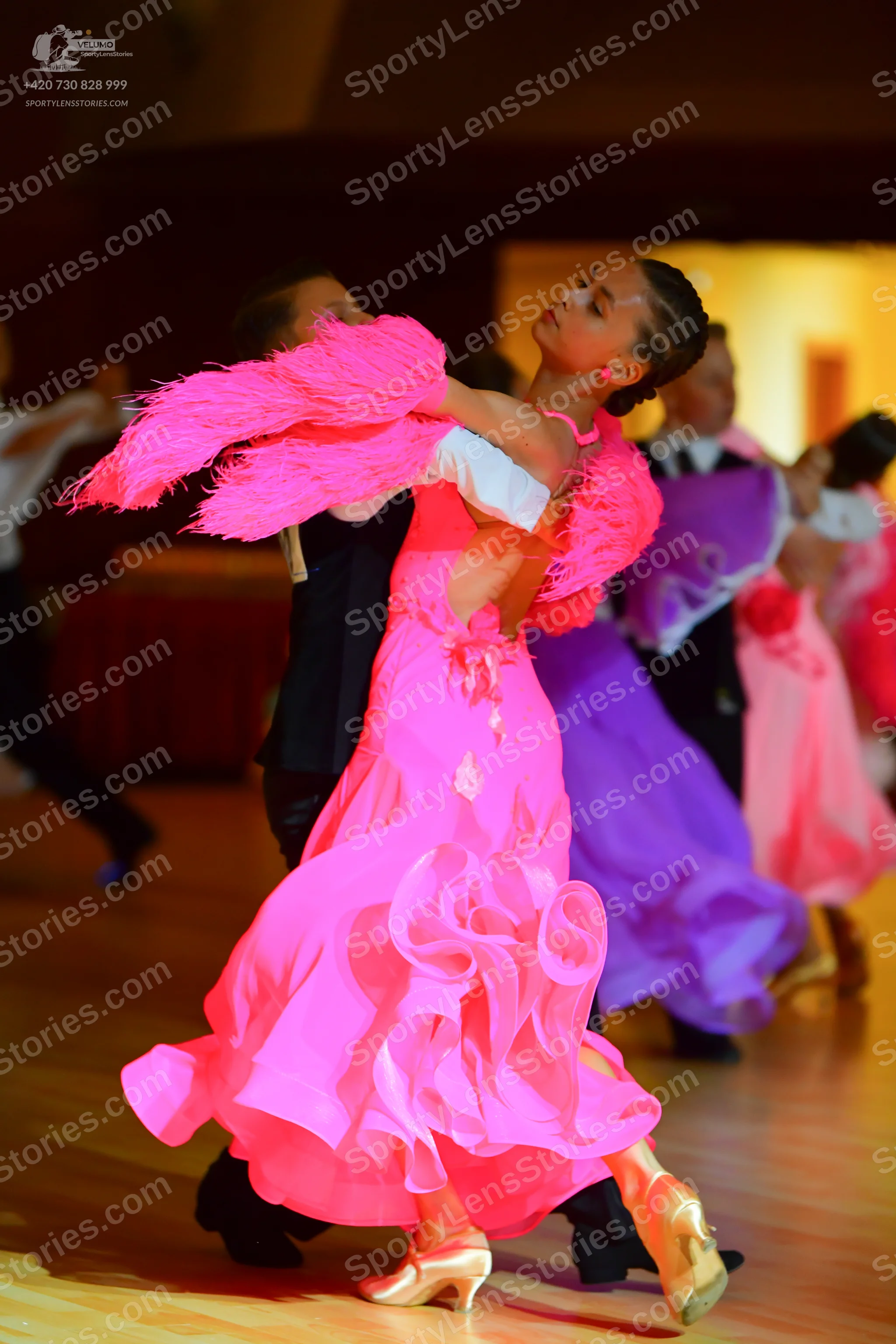 Dancesport competitor: Female dancer in foreground: bright pink ballgown with a voluminous ruffled skir