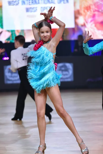 Dancesport competitor: Female dancer: cyan Latin dance dress with heavy fringe and pink floral accents