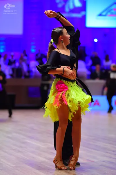 Dancesport competitor: Female dancer: black long-sleeved top and neon yellow/green fringed skirt with p