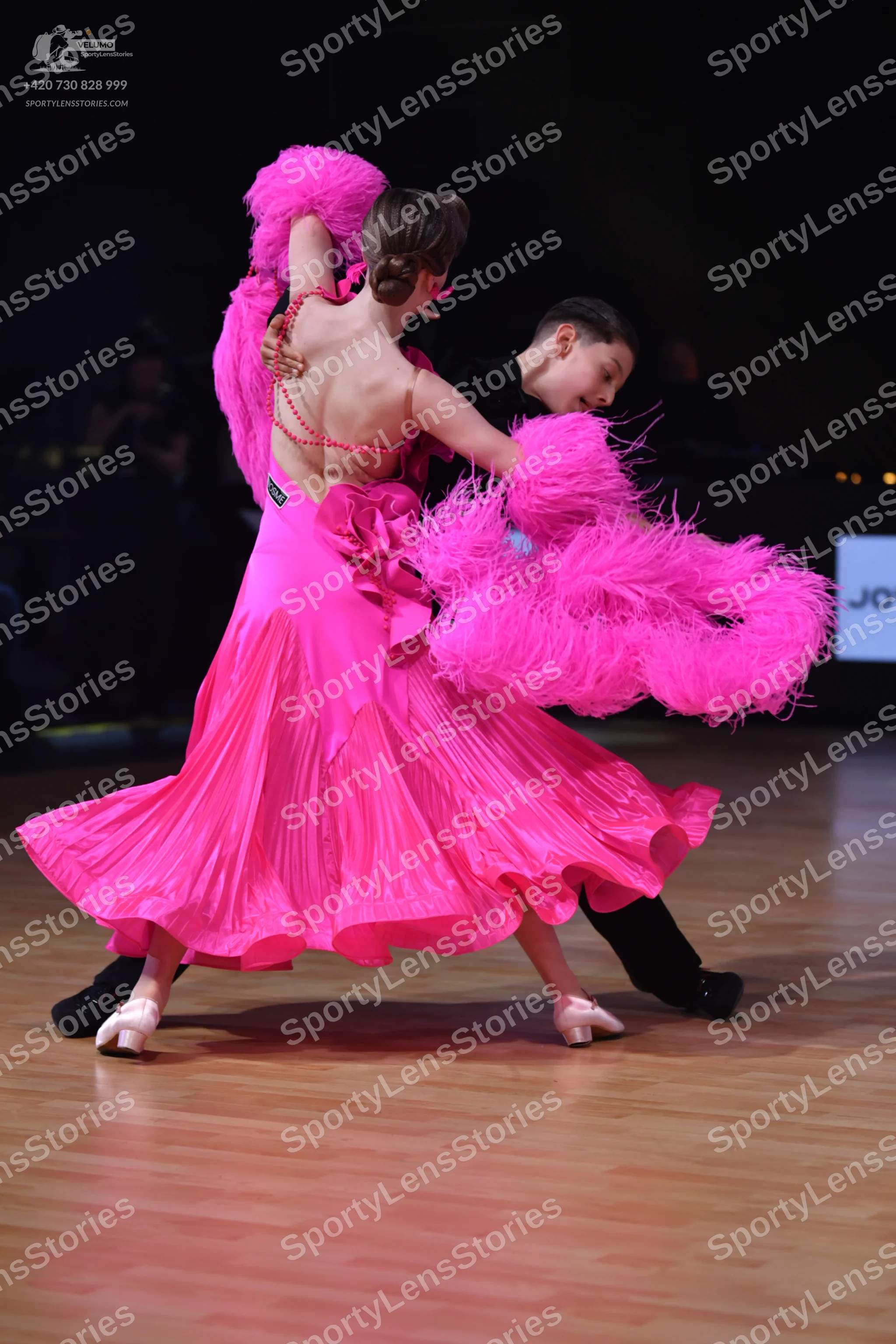 Dancesport competitor: Female dancer: bright pink ballroom dress with a full, pleated skirt, backless d