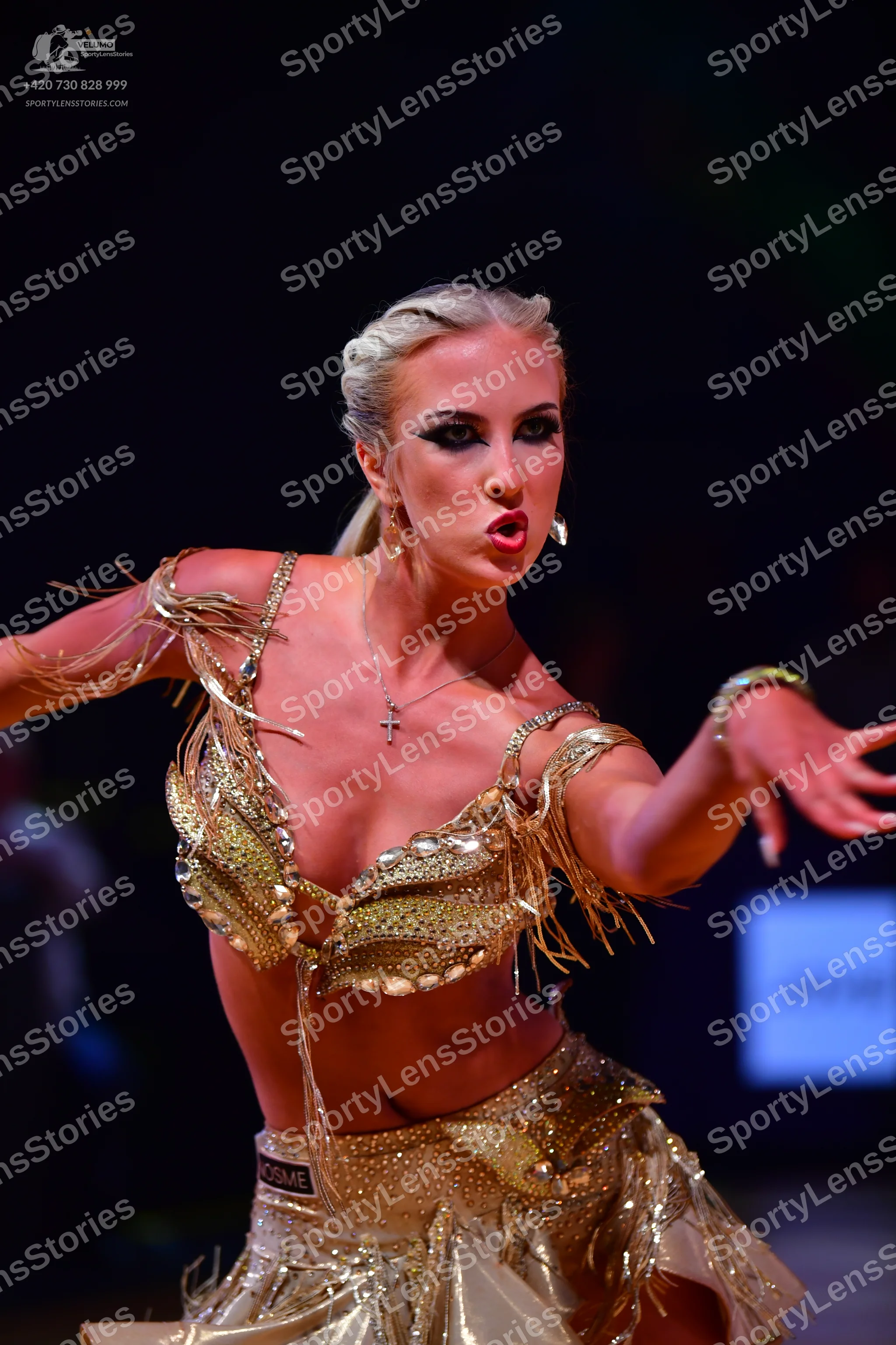 Dancesport competitor: Female dancer: gold Latin dance costume decorated with sequins, gems, and long f