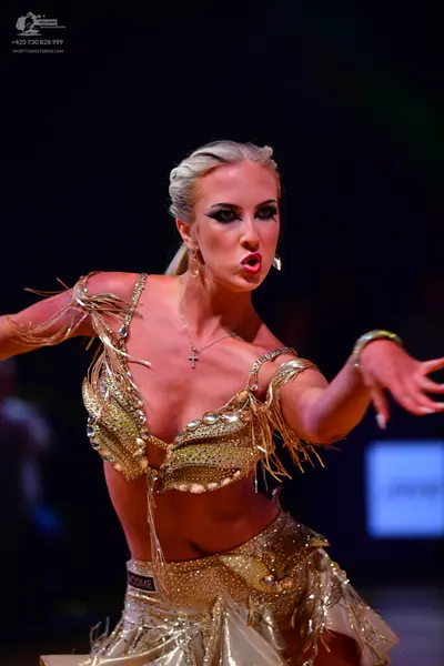 Dancesport competitor: Female dancer: gold Latin dance costume decorated with sequins, gems, and long f