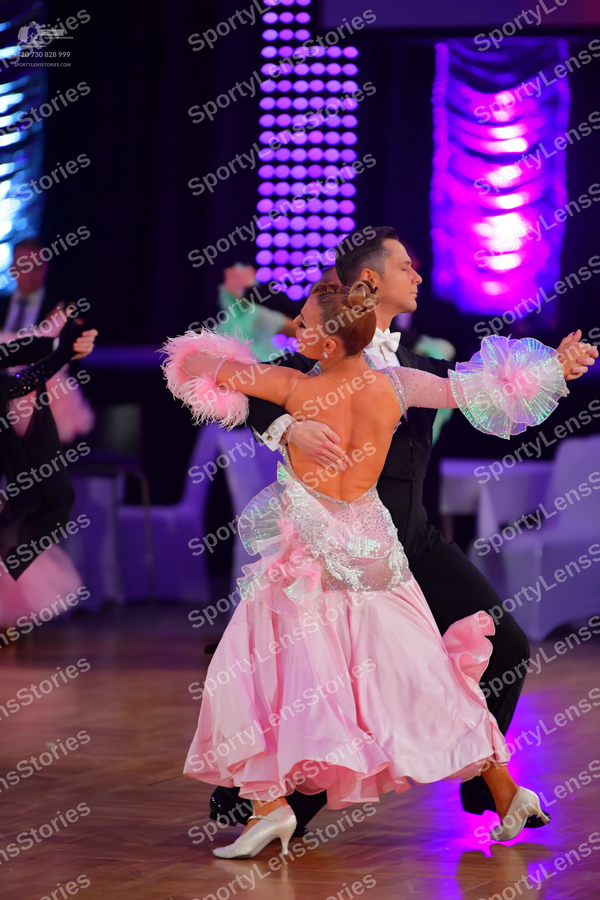 Dancesport competitor: Female dancer in foreground: light pink ballgown with a silver sequined bodice a