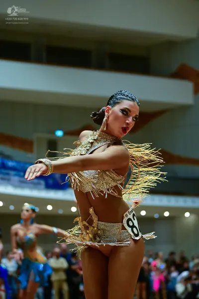 Dancesport competitor: Female dancer in foreground: gold latin dress with sequins and long fringe, and 