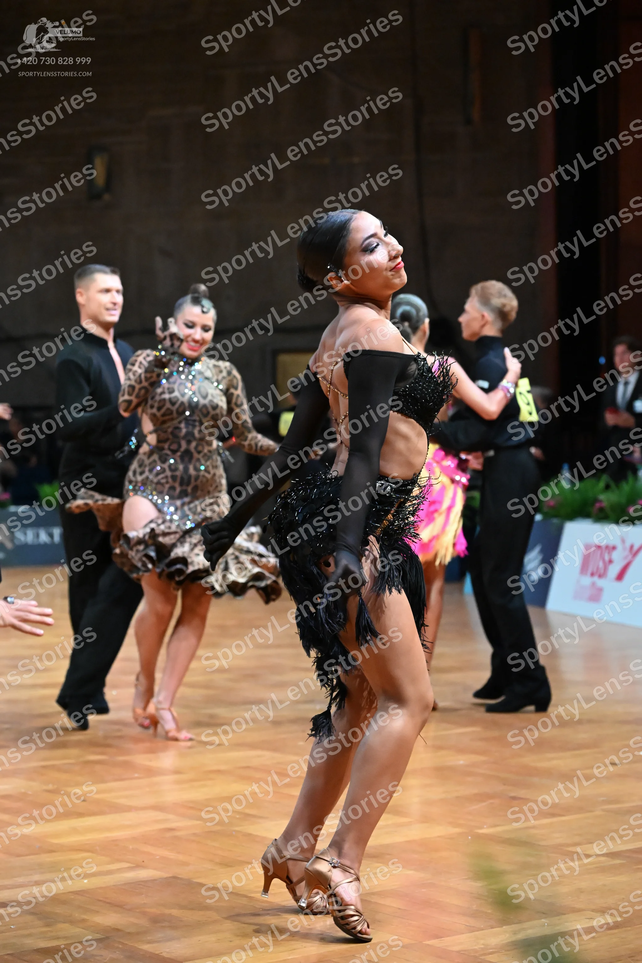 Dancesport competitor: Female dancer in foreground: black latin dress with fringe and long black gloves