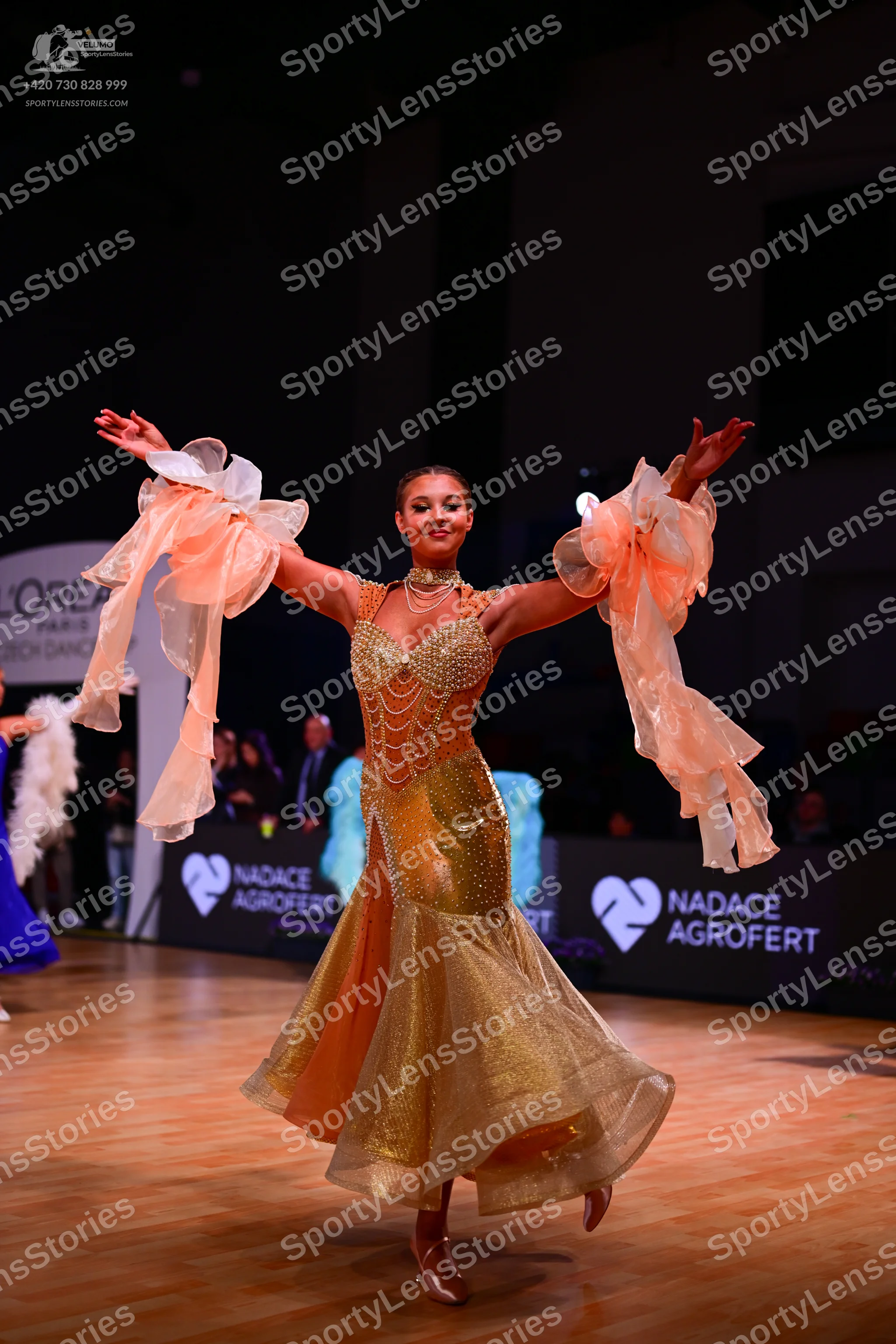 Dancesport competitor: Female dancer: gold ballroom dress with a sequined bodice and a voluminous, mult