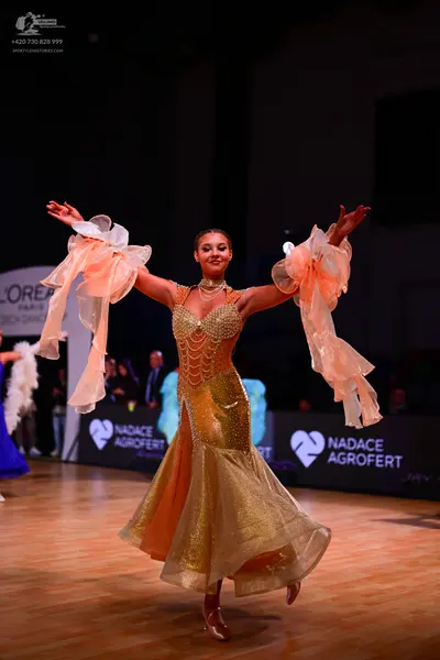 Dancesport competitor: Female dancer: gold ballroom dress with a sequined bodice and a voluminous, mult