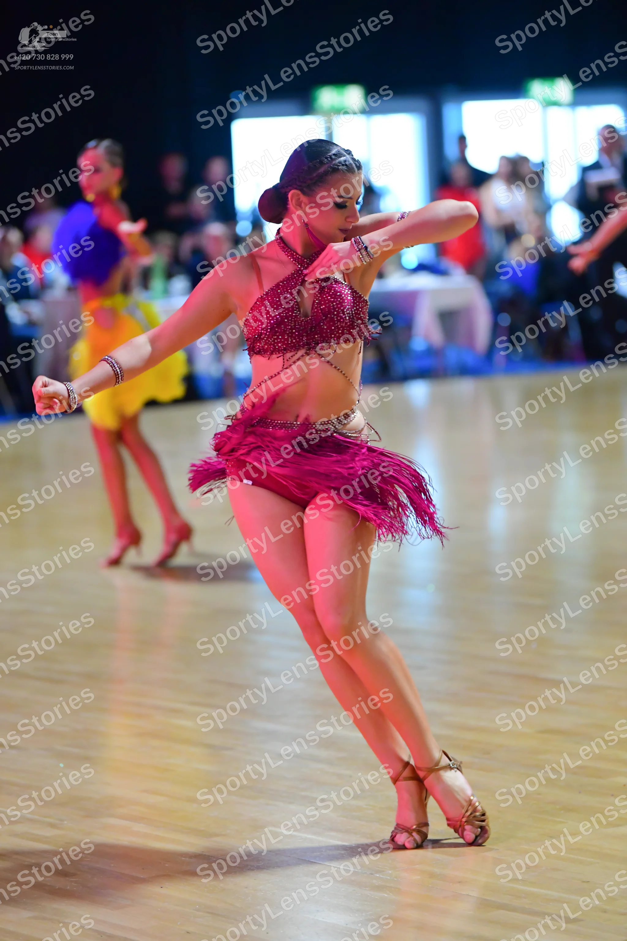 Dancesport competitor: Foreground dancer: magenta two-piece Latin costume featuring a sequined halter t