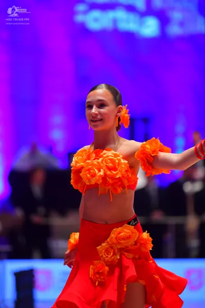 Dancesport competitor: Female dancer: orange two-piece Latin costume featuring a crop top and a skirt, 