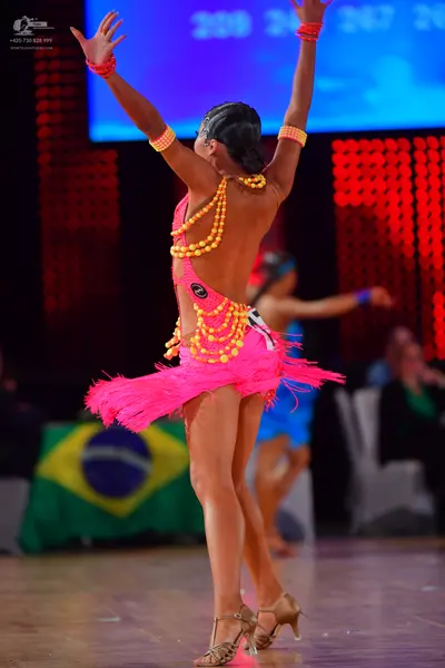 Dancesport competitor: Female dancer in foreground: bright pink Latin dress with long pink fringe and y