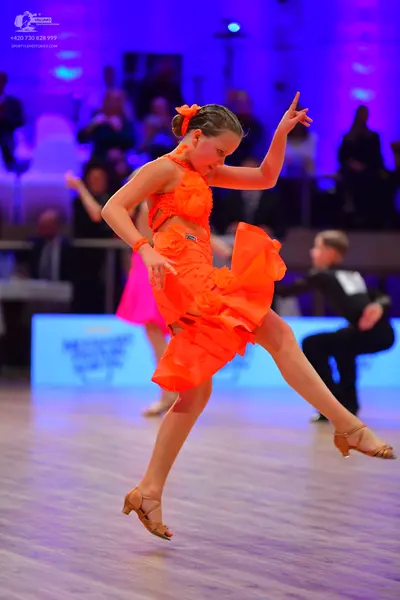 Dancesport competitor: Female dancer: orange Latin dance dress with a ruffled skirt and halter neckline