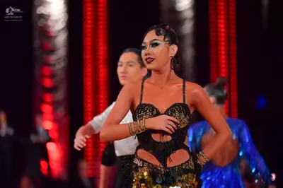 Dancesport competitor: Female dancer in foreground: black latin dress with gold sequins, cutouts, and t