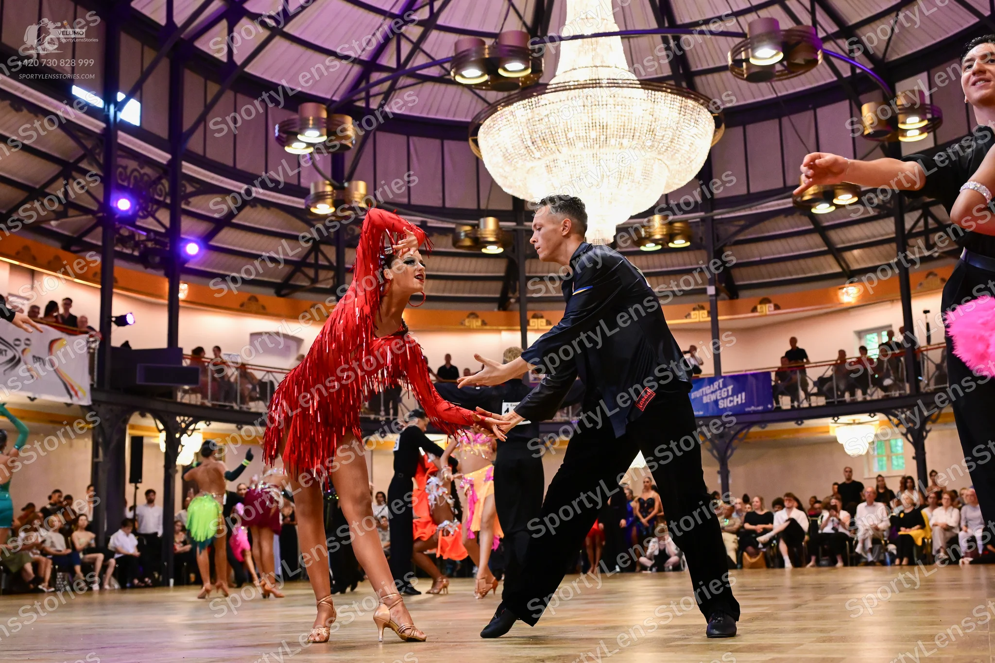 Dancesport competitor: Female dancer in foreground: red Latin dress with fringe