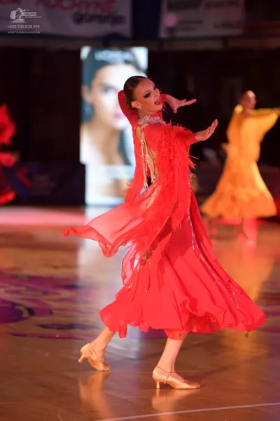 Dancesport competitor: Female dancer in foreground: bright red, long, flowing ballroom dress with fring