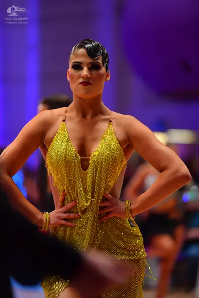 Dancesport competitor: Female dancer: gold sequined latin dress with thin straps and a deep V-neckline,