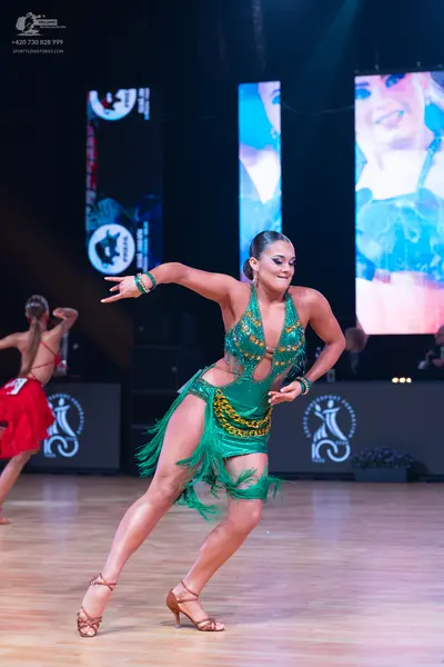 Dancesport competitor: Female dancer (foreground): green latin dress with gold sequin embellishments an