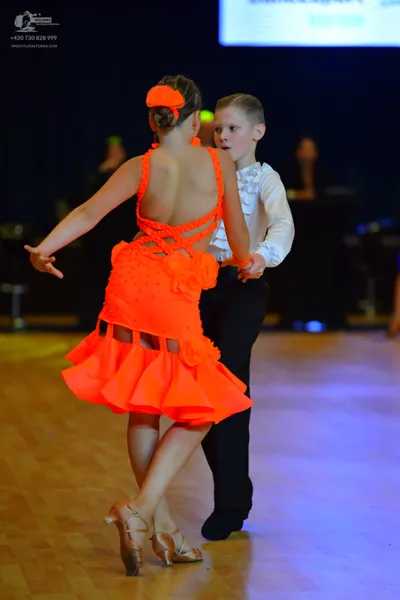 Dancesport competitor: Female dancer: bright orange Latin dance dress with thin straps and a ruffled, l