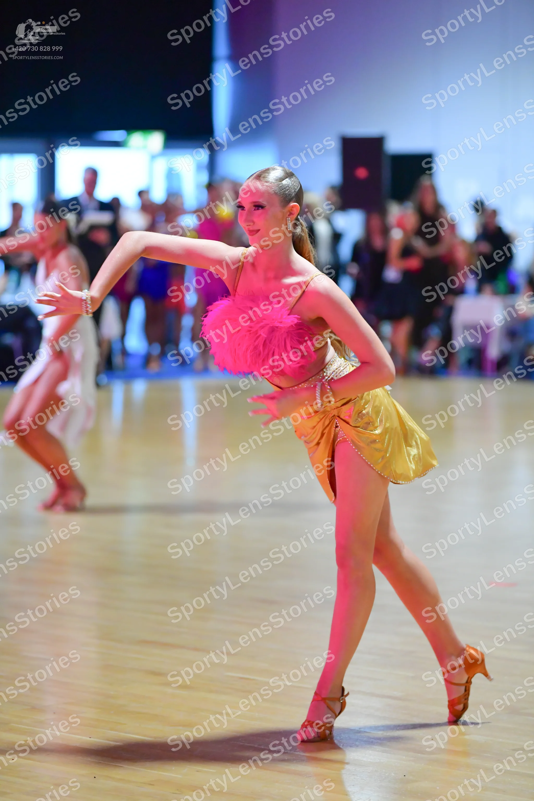 Dancesport competitor: Female dancer (foreground): pink and gold Latin dance dress with a textured pink