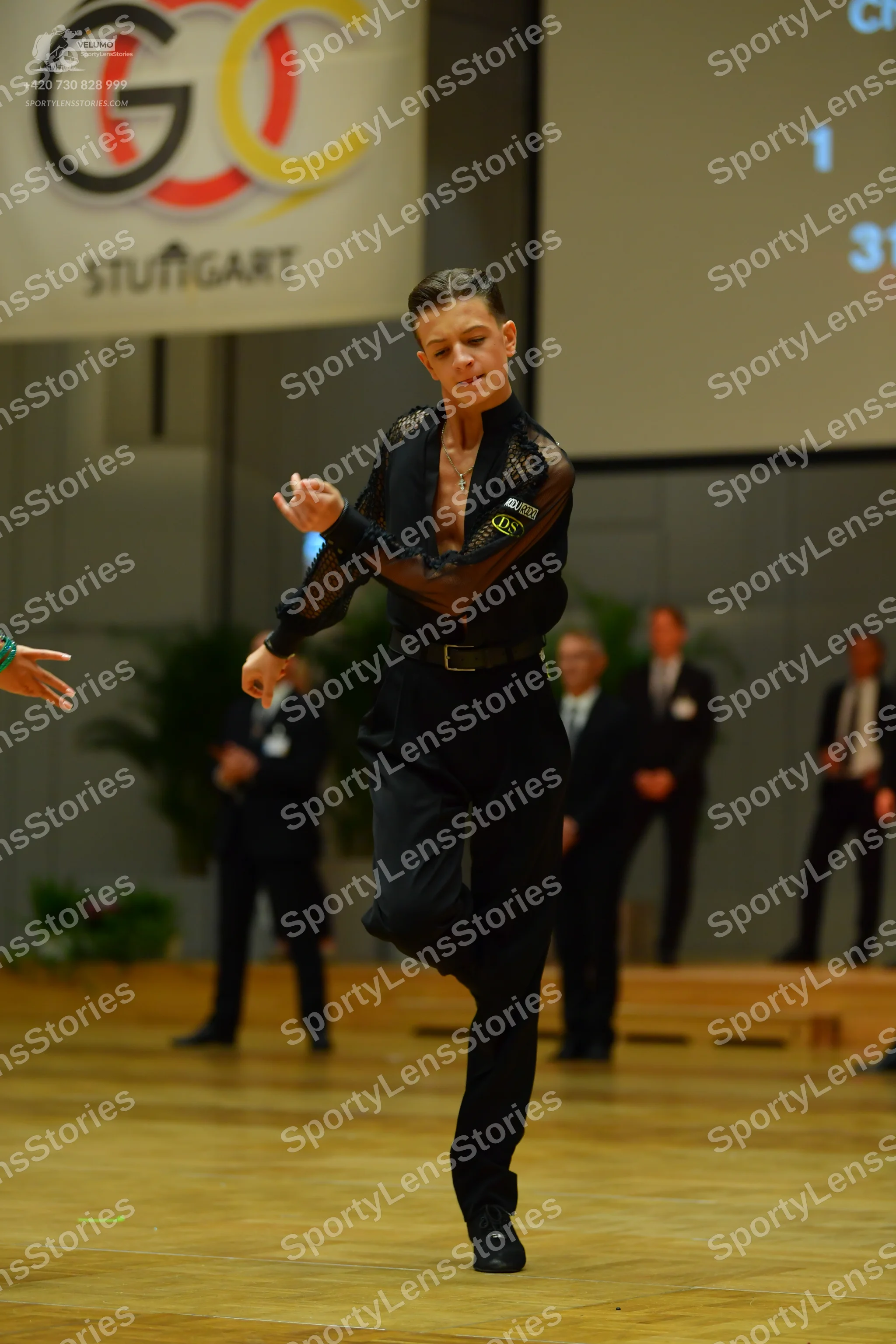 Dancesport competitor: Male dancer in foreground: black long-sleeved top with sheer mesh sleeves and up