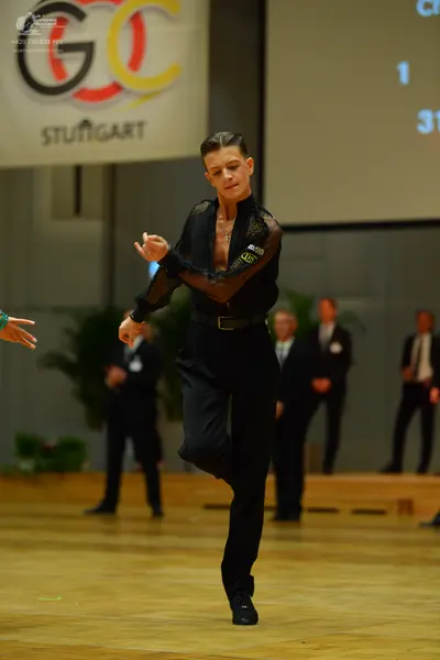 Dancesport competitor: Male dancer in foreground: black long-sleeved top with sheer mesh sleeves and up