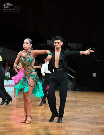 Dancesport competitor: Female dancer: teal and bright pink latin dance dress with sequins, lace, and fr
