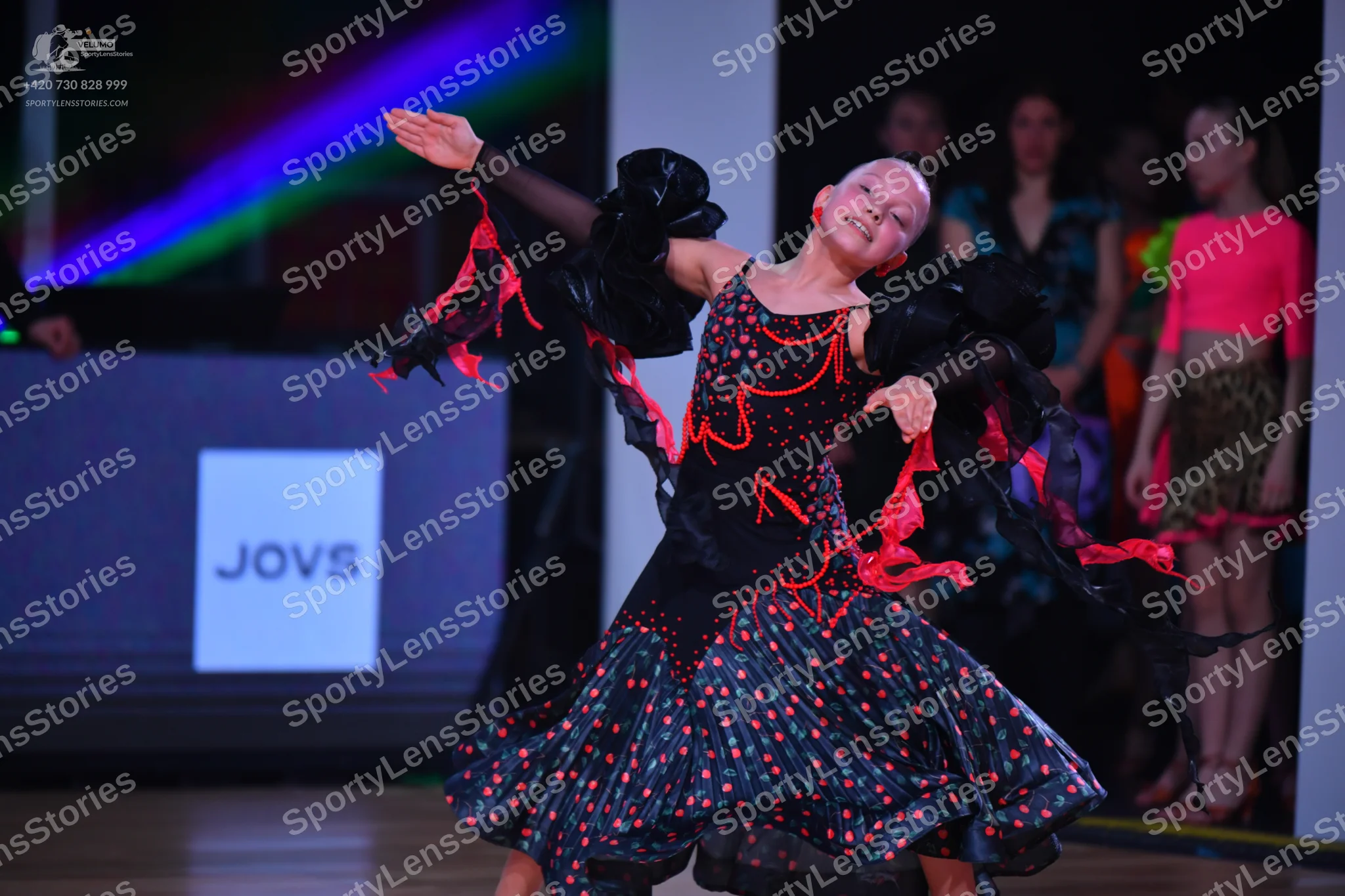 Dancesport competitor: Main dancer: black Latin dance dress with red/coral patterns and sequins, featur