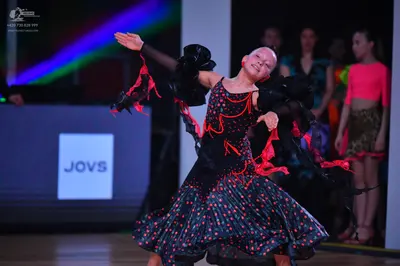 Dancesport competitor: Main dancer: black Latin dance dress with red/coral patterns and sequins, featur